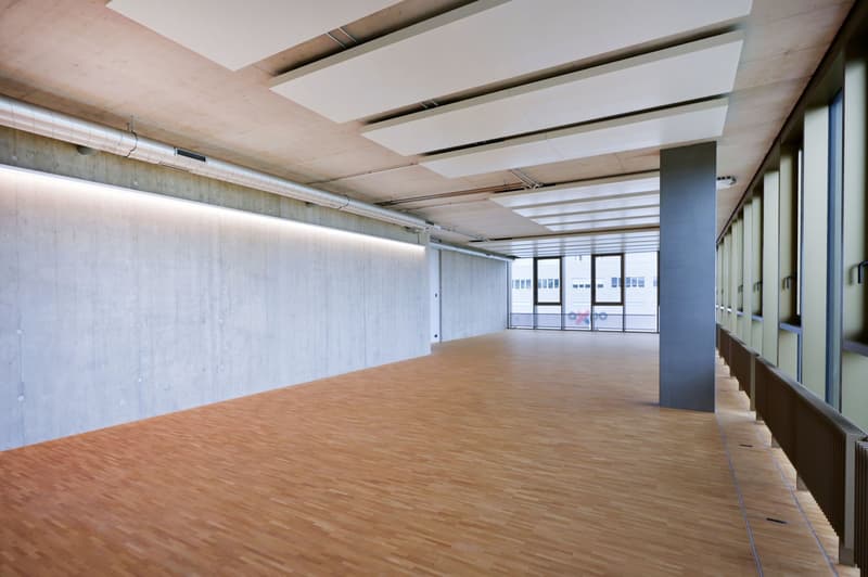Empty room with wooden floor, concrete walls, large windows, and a central column