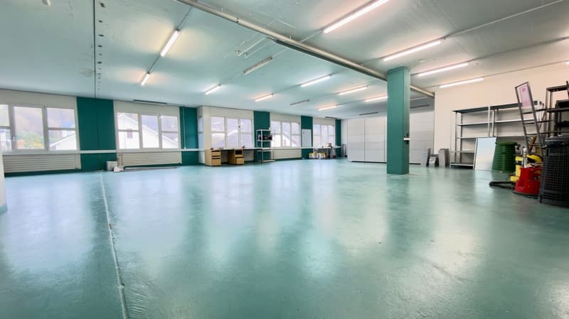 spacious room with green walls and white ceiling, fluorescent lighting, several windows, white floor, shelves, storage boxes, and items