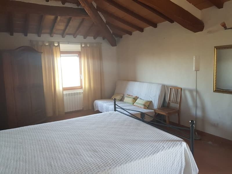Spacious bedroom with wooden beamed ceiling, white walls, large window, queen-size bed, sofa, and wooden furniture.