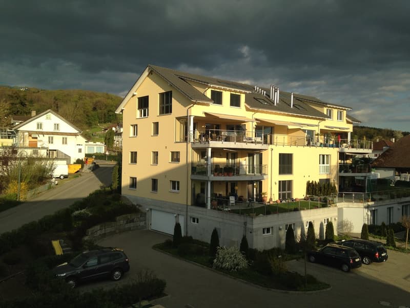 Yellow apartment building with solar panels, multiple balconies, garages and cars parked in front