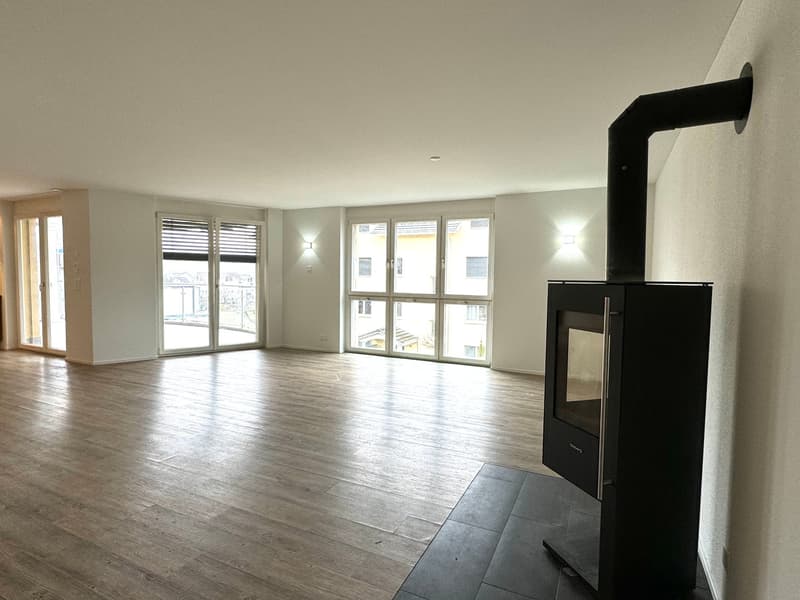 Empty room with hardwood floors, large windows, and a modern fireplace.