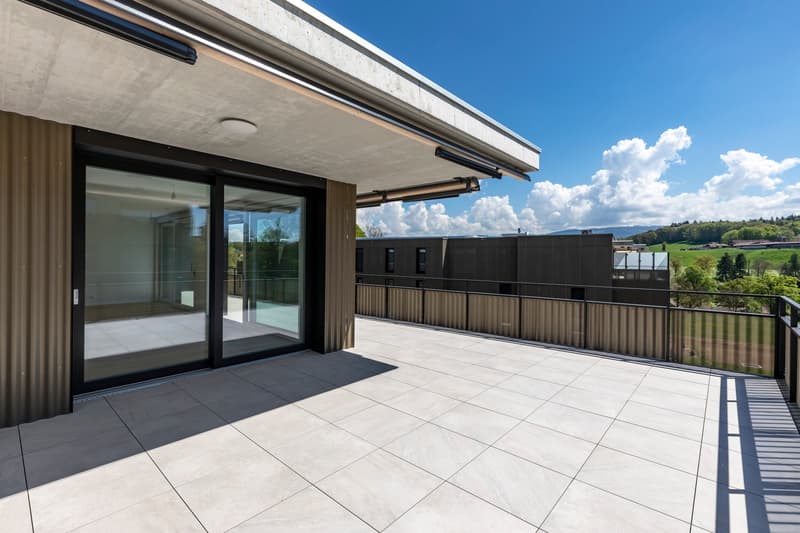 Large balcony or terrace with glass railing, sliding glass doors leading to the interior, modern tiled flooring, and scenic views of the surrounding countryside.