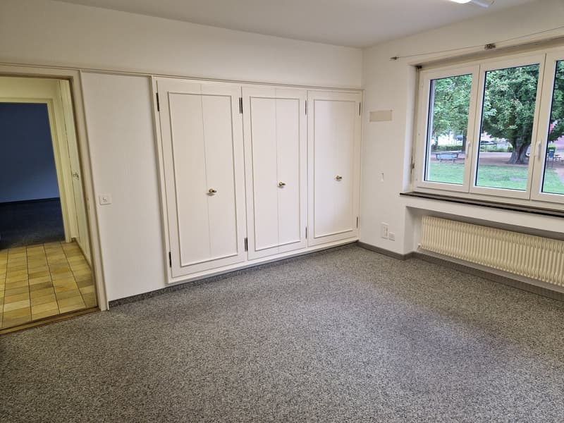 Spacious bedroom with white built-in wardrobes, hardwood flooring, and large windows overlooking a garden area.