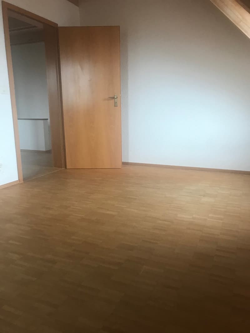 Empty room with wooden floor, white walls, two doors, and a power outlet on the left wall.