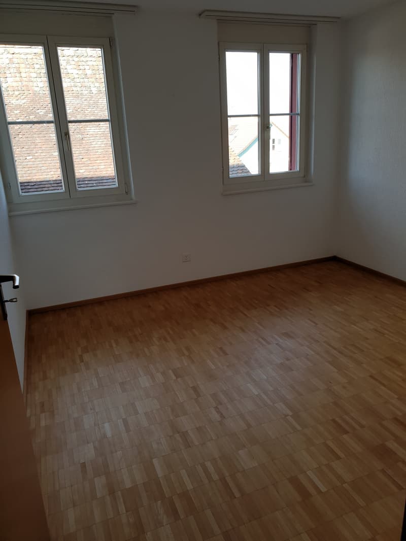Empty room with wooden floor, two windows, white walls, power outlet