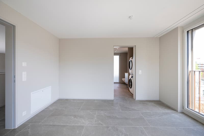 Empty room, tiled floor, two washing machines in separate room, balcony