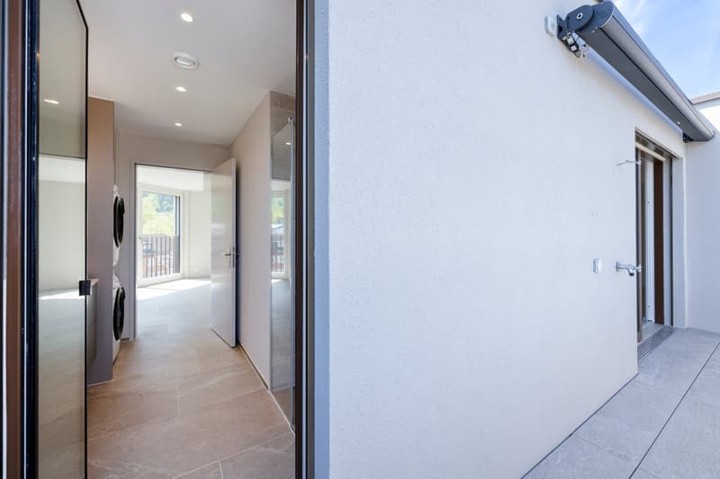 Wide entrance with glass door, tiled floor, large mirror, indoor laundry machines