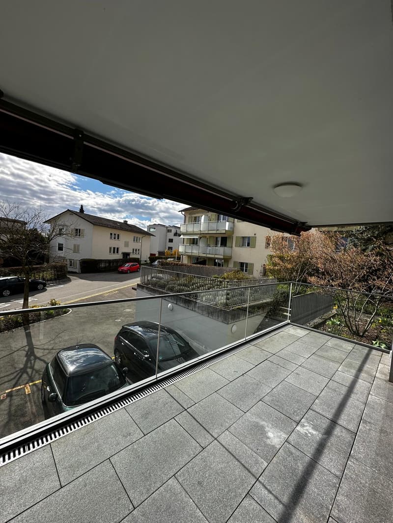 Balcony with glass railing, view of parking lot and buildings