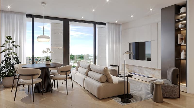 The image shows a modern and spacious open-plan living room and dining area with large windows offering a scenic view. The living room features a comfortable beige sofa with decorative pillows, a wall-mounted TV, and a shelving unit. The dining area has a