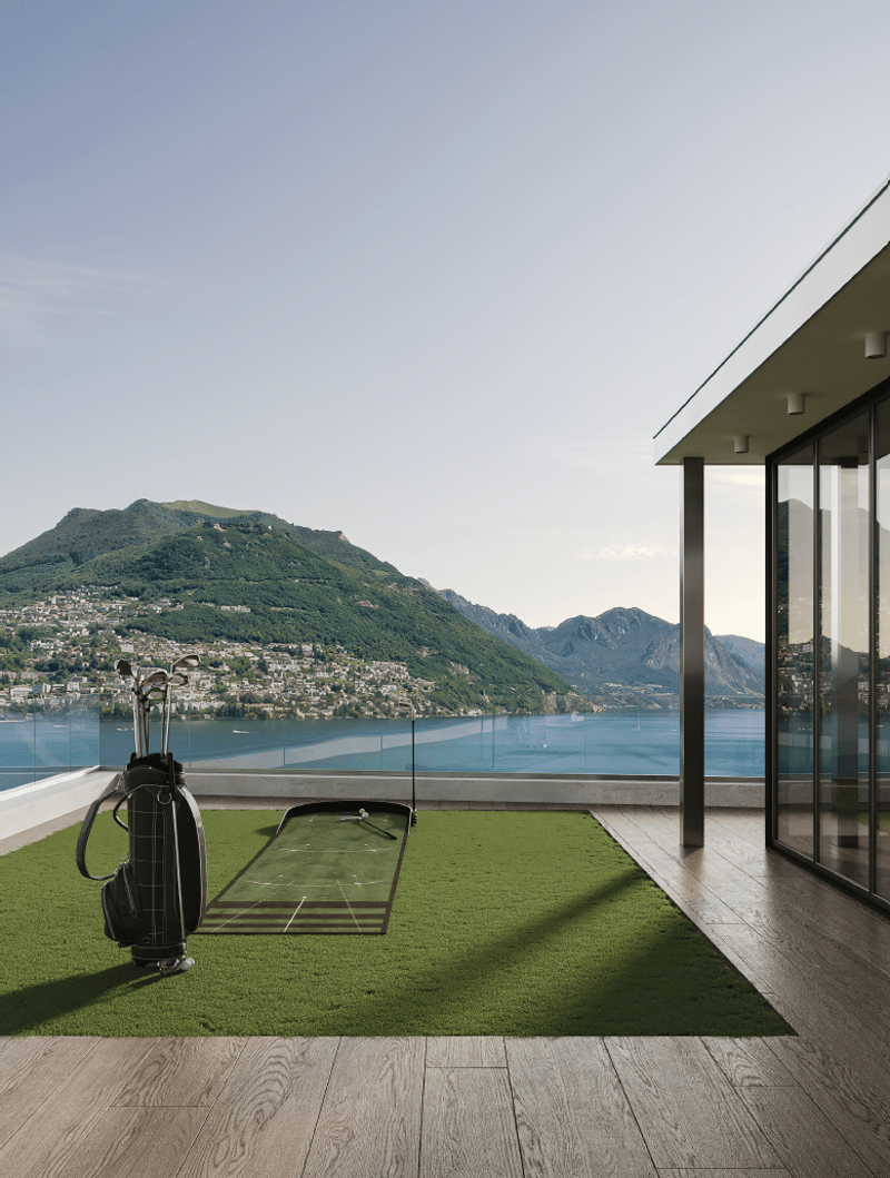 Luxury villa with a panoramic view of a lake surrounded by mountains. The property features a balcony or terrace with a putting green and golf bag, allowing the owner to practice their golf skills while enjoying the stunning natural scenery.