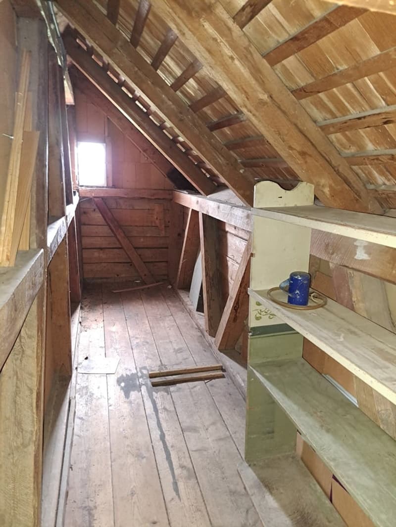 Wooden attic space with slanted roof, wooden beams, and old wooden shelves and storage items