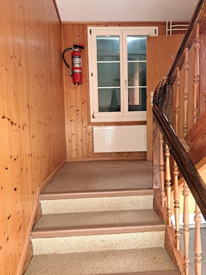 Wooden staircase with a fire extinguisher mounted on the wall, leading to a window with a wooden frame