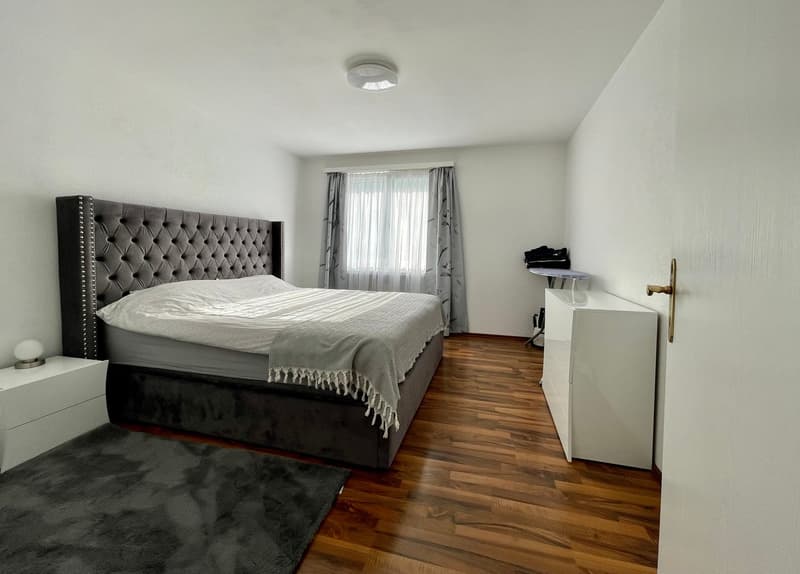 Bedroom with bed, nightstand, rug, and cabinet. White walls and wooden floor.