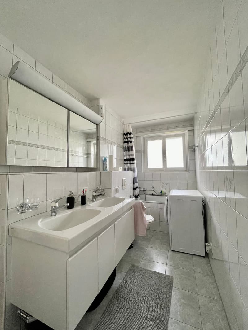 modern bathroom with white tiles, double sink, mirror, bathtub, toilet, washing machine