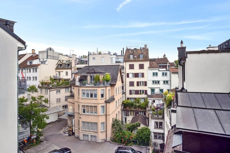The image shows a cityscape with a mix of old and new buildings. There are several multi-story residential and commercial buildings with balconies and terraces visible. The buildings have a variety of architectural styles, including some with traditional