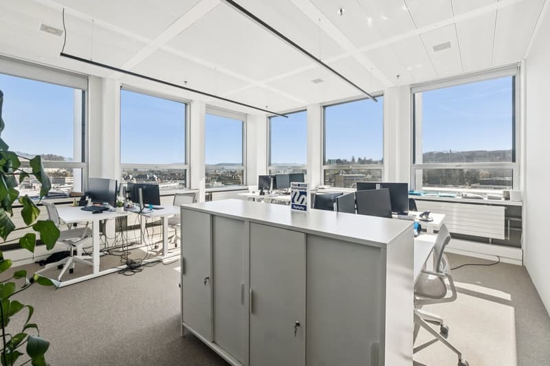 modern office with large windows, white desks, computer monitors, office chairs, white cabinets, carpeted floor, plant
