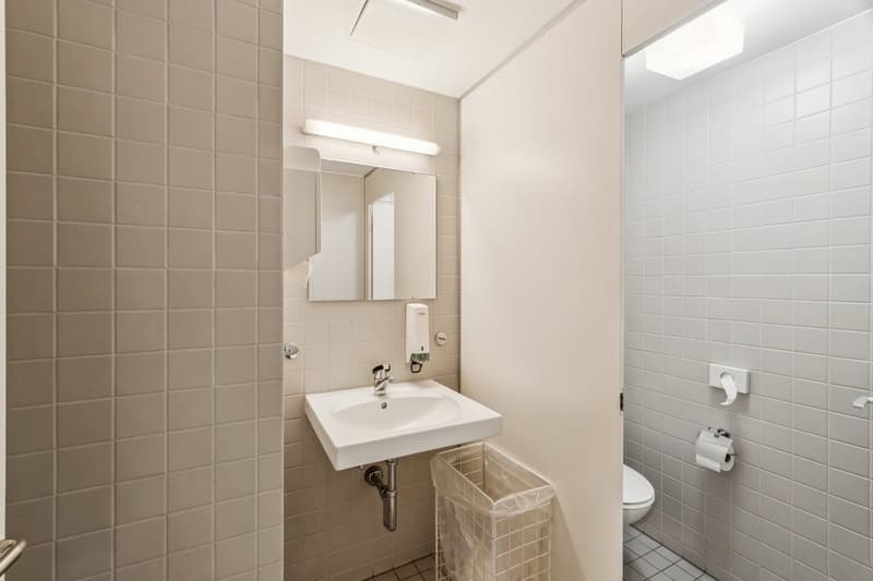 Bathroom with white tiles, sink, mirror, toilet, and trash bin