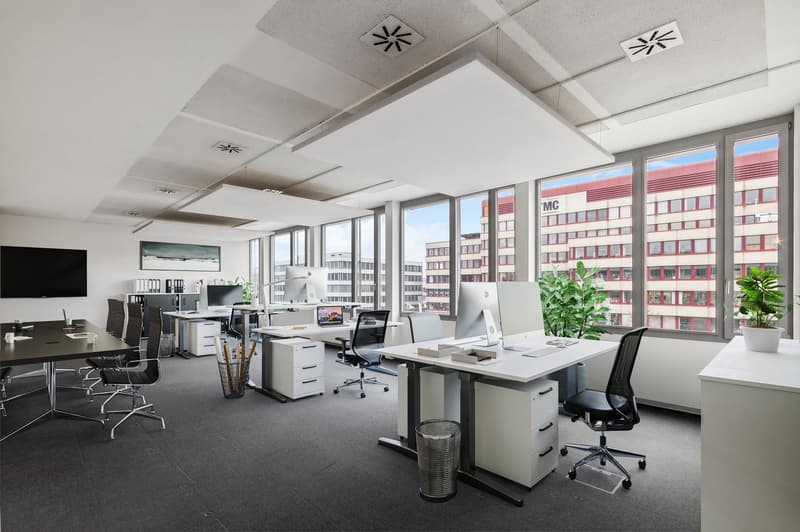 modern office space with desks, chairs, monitors, plants, trash bins, and large windows