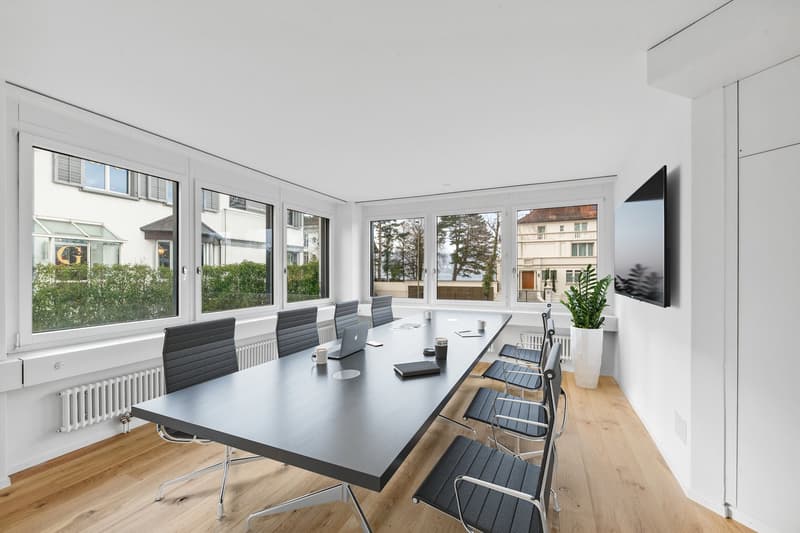 modern office room with large windows, wooden floor, long table, chairs, radiator, TV, plant