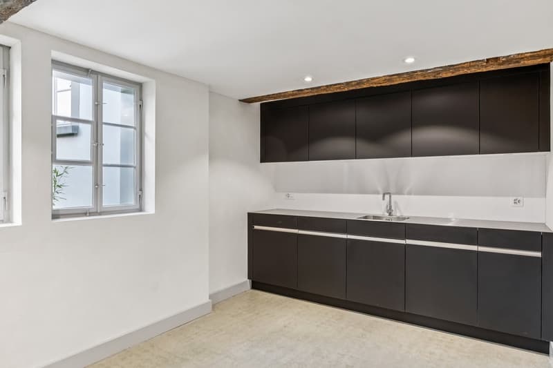 modern kitchen with white walls, black cabinets, stainless steel countertop, sink, faucet, and power outlets