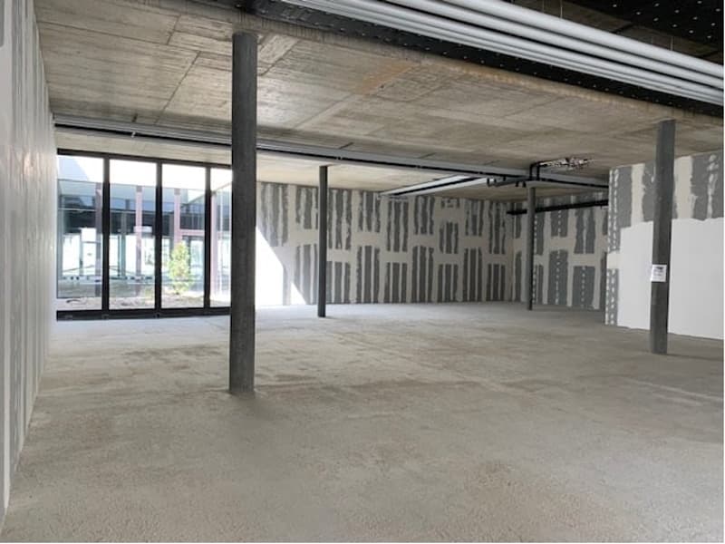 Large open space with concrete floor, exposed ceiling beams, and large windows providing natural light. The space appears to be a commercial or industrial property, likely intended for retail, office, or other commercial use.
