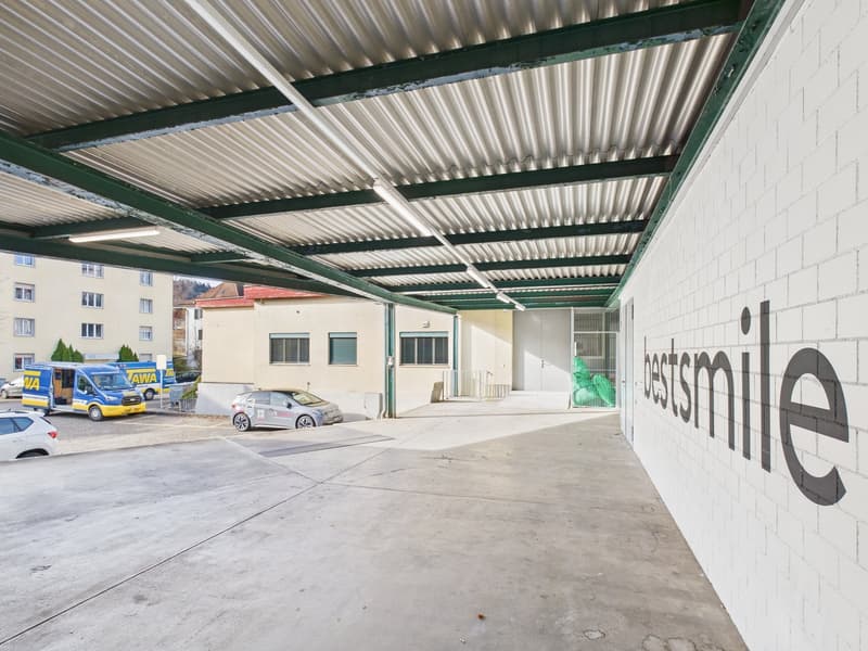Garage with covered entrance, several cars parked, brick building in the background, white wall with the word 'bestsmile' on it