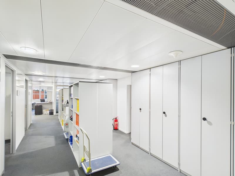 a long hallway with white walls, gray flooring, built-in white shelves, and a trolley