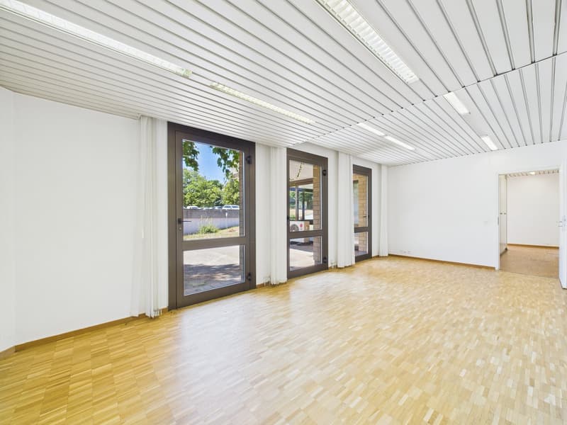 Empty room with white walls, wooden flooring, two glass doors, and three open doors with a view of a courtyard