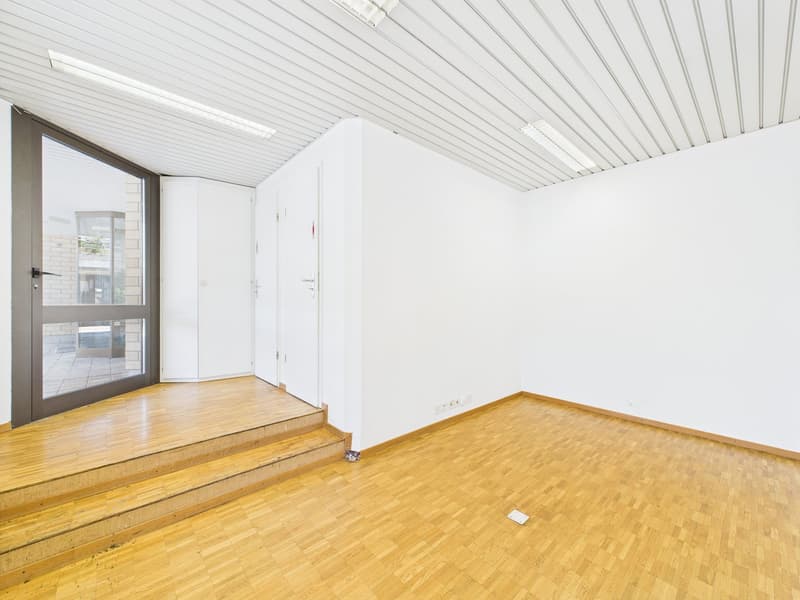 Empty room with white walls, wooden floor, and a glass door leading to an outdoor area. The ceiling has a white paneled design.