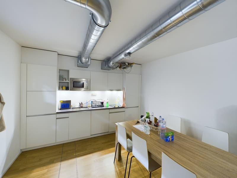 kitchen has white cabinets, wooden table, white chairs, microwave, sink, countertop, bottles, baskets