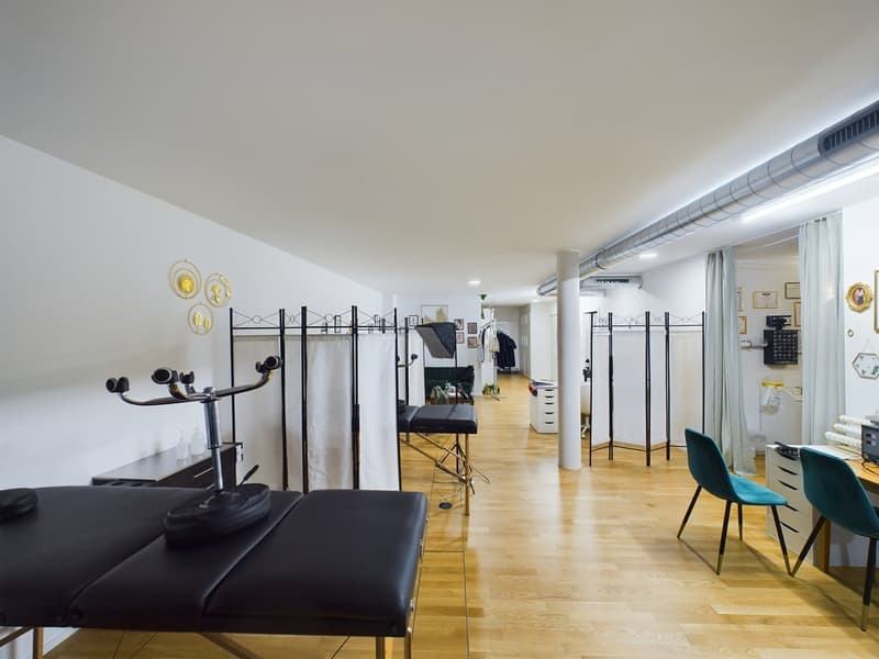 Rehabilitation room with medical equipment, cabinets, desk, and chairs. Wooden floor and white walls.