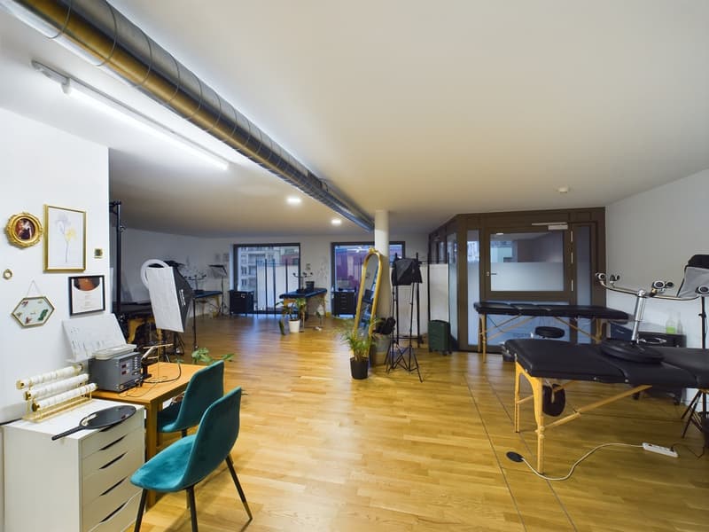 large room, wooden floor, white walls, several picture frames, massage tables, stools, plants, lamps, chair, desk