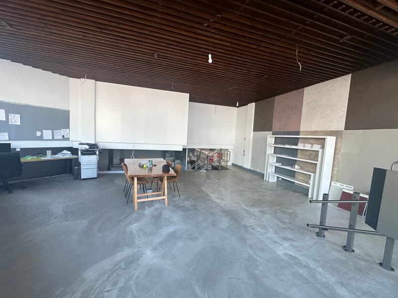 Large empty room, wooden ceiling, tables, office equipment, empty shelves, plain flooring