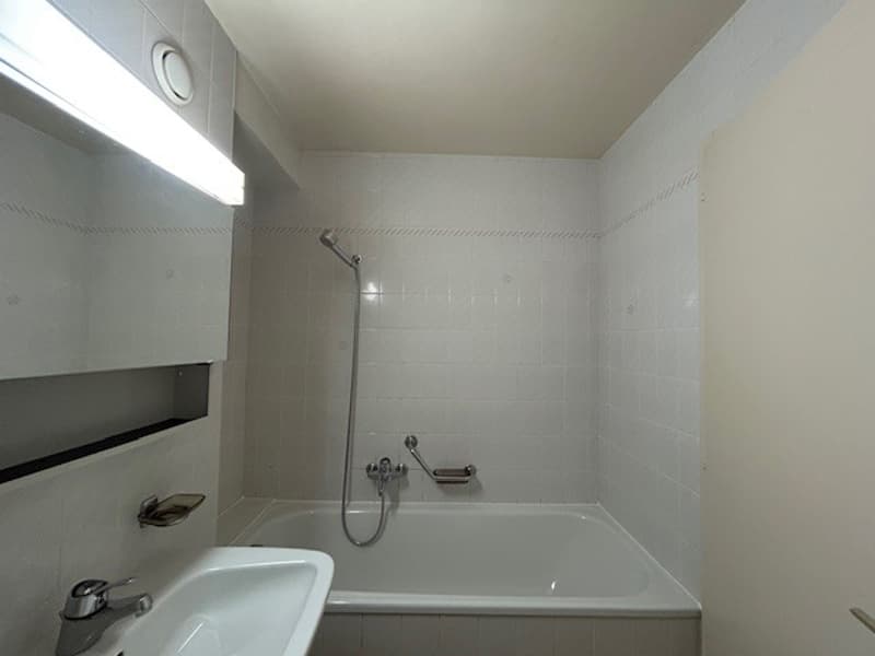 The image shows a bathroom with a white bathtub, a shower head, and white walls.
