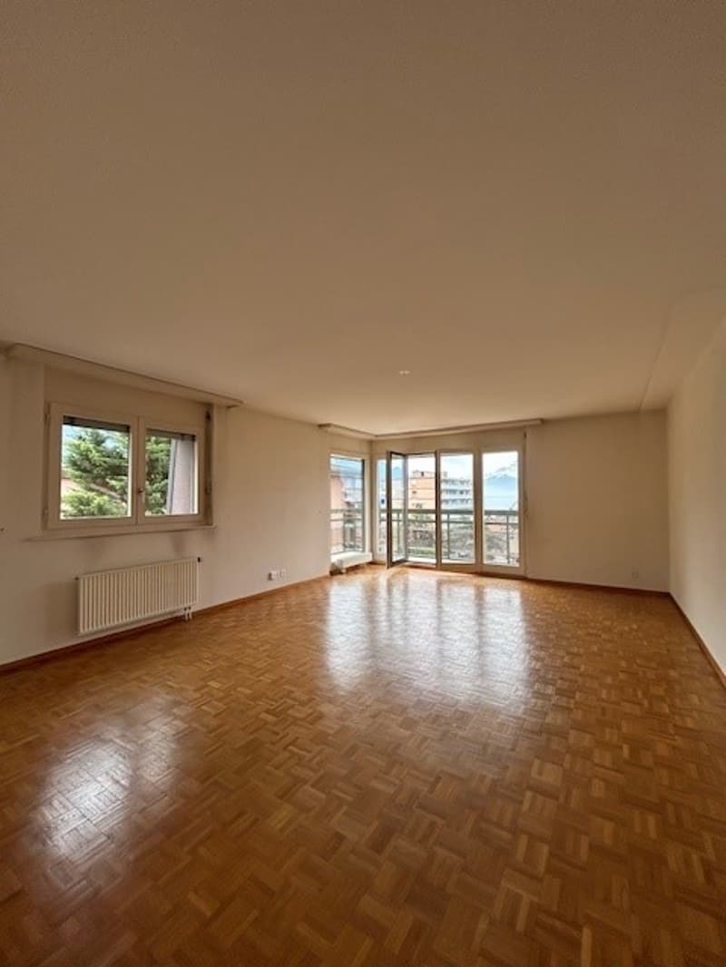 Spacious living room with hardwood flooring, large windows, and access to a balcony or terrace.