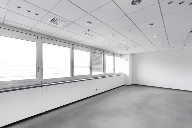 large empty room, white walls, white ceiling, gray floor, long windows, closed shutters