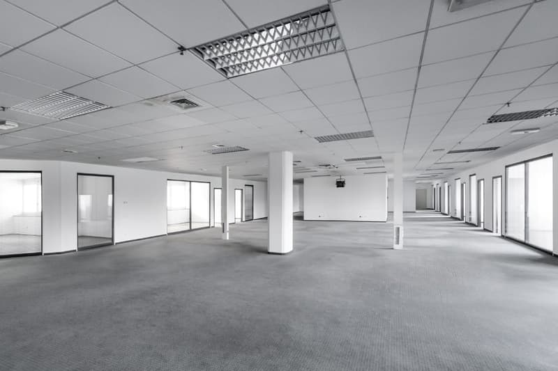 Empty office room with white walls, tiled floor, large windows, pillars, ceiling lights