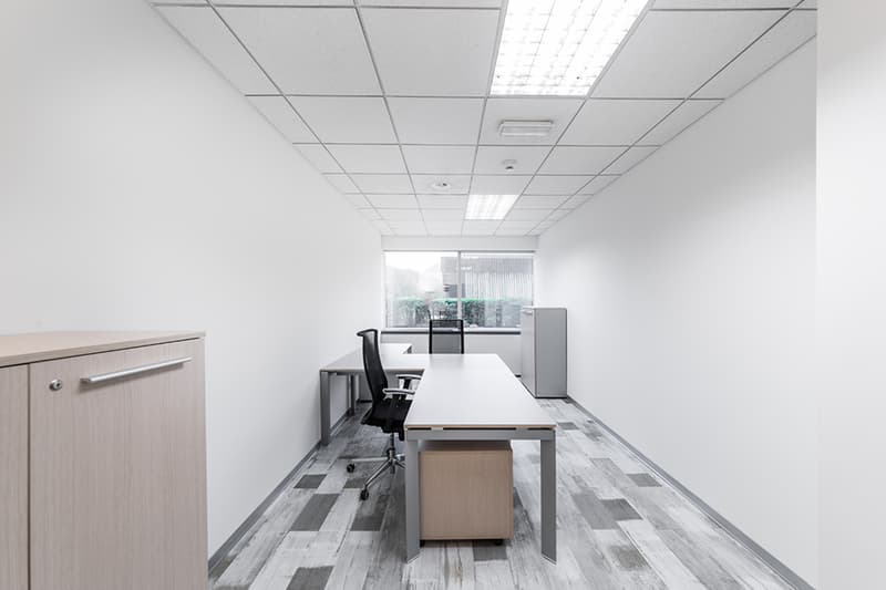 An empty room with white walls, a tiled floor, a window, two desks, and a cabinet.