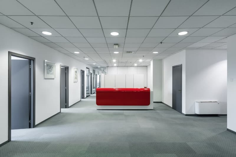 office corridor, white walls, grey floor, red reception desk, grey doors, ceiling lights