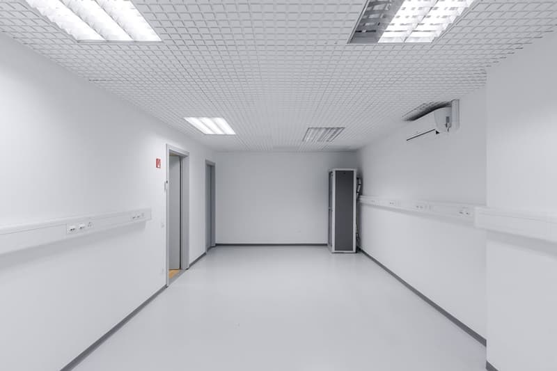 Empty room with white walls and ceiling, two doors, two lights, and an air conditioner.