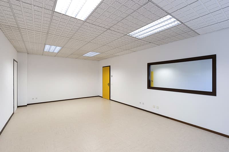 Empty room with white walls, yellow door, light gray floor, mirror on wall, electrical outlets