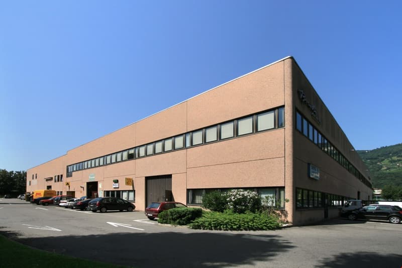 Business building, multiple windows, large parking lot, logo sign on side, cars parked in front.
