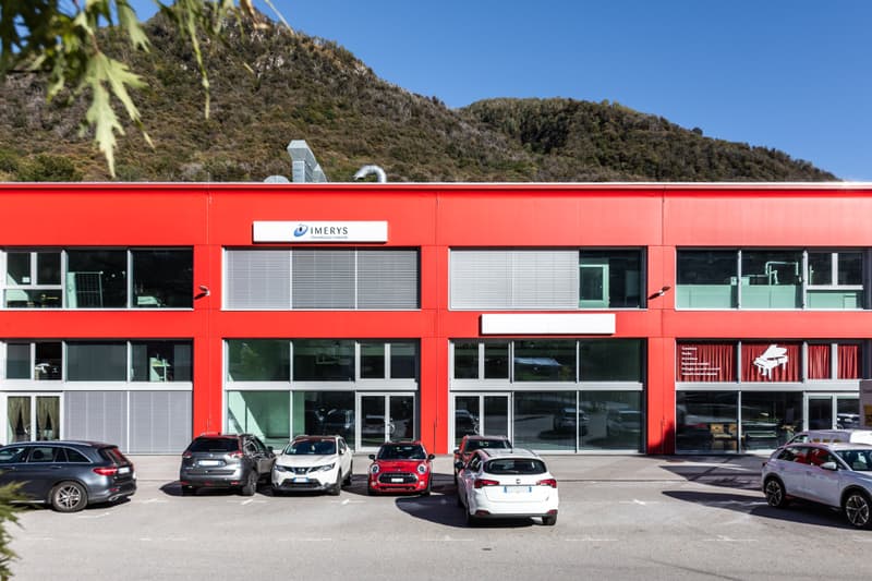Modern red building, multiple windows, glass entrance doors, several cars parked in front