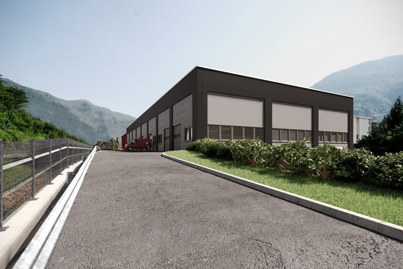 Industrial building with multiple garage doors, surrounded by greenery and mountains