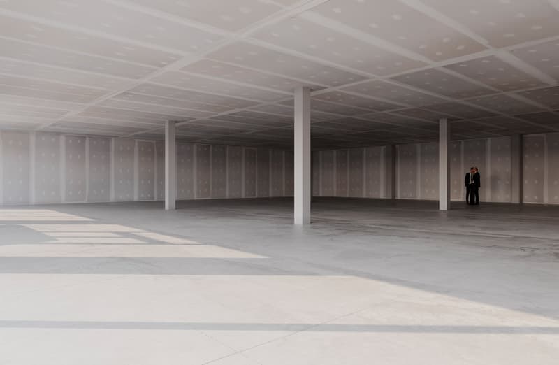 Empty room with white walls, ceiling, and floor, three pillars, two people standing in the corner