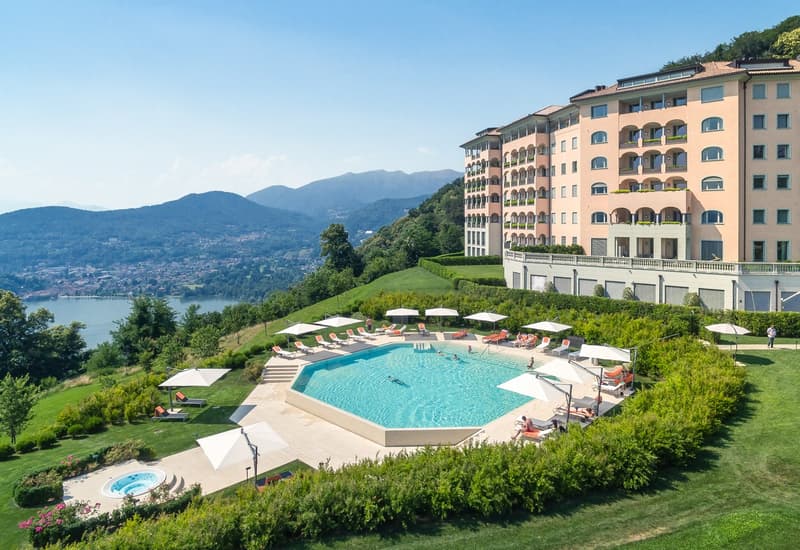 Hillside resort with pool, lounge chairs, umbrellas, and mountains in the background