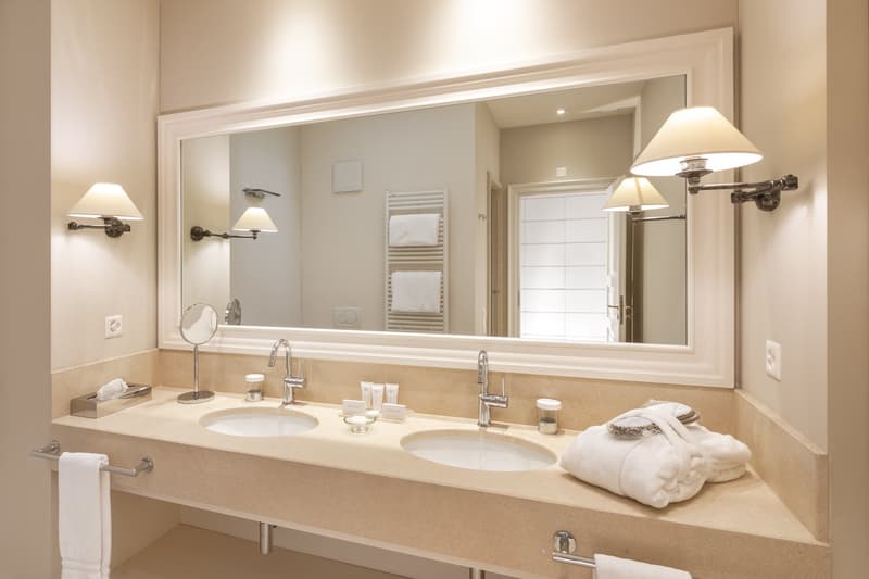Double sink, large mirror, two lamps on either side of mirror, towel holder on wall