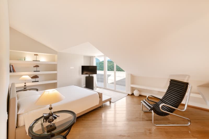 ample room with wooden floors, bed, bedside lamps, glass coffee table, wall shelves with decorations, tv, white walls, large windows leading to a balcony, breathtaking view