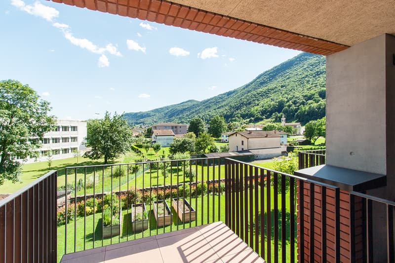 Balcony overlooking a scenic mountain landscape with a village below, surrounded by lush greenery and trees