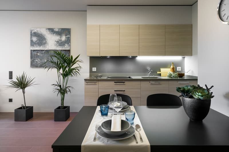 Modern kitchen with light wood cabinets, black countertops, stainless steel appliances, and a dining table with place settings